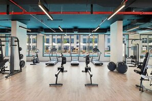 Ein modernes Fitnessstudio mit Cardiogeräten, Kurzhanteln und Blick auf einen Pool sowie Gebäude.