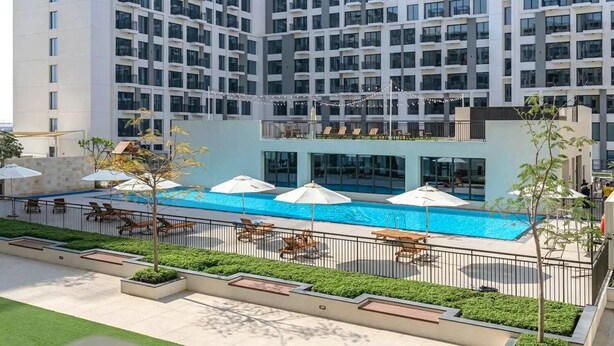 Un hotel de varios pisos con piscina en la azotea, mobiliario exterior y un jardín bien cuidado.