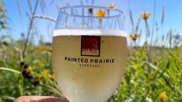 A hand holding a glass with 'Painted Prairie Vineyard' label, set against a natural outdoor background.
