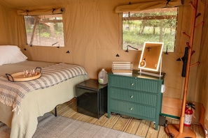Quarto com tenda, com uma cama, mesa de cabeceira, penteadeira, espelho e janela com vista para árvores.