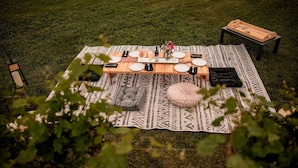 An outdoor dining setup with a table, chairs, and a blanket on a grassy field.