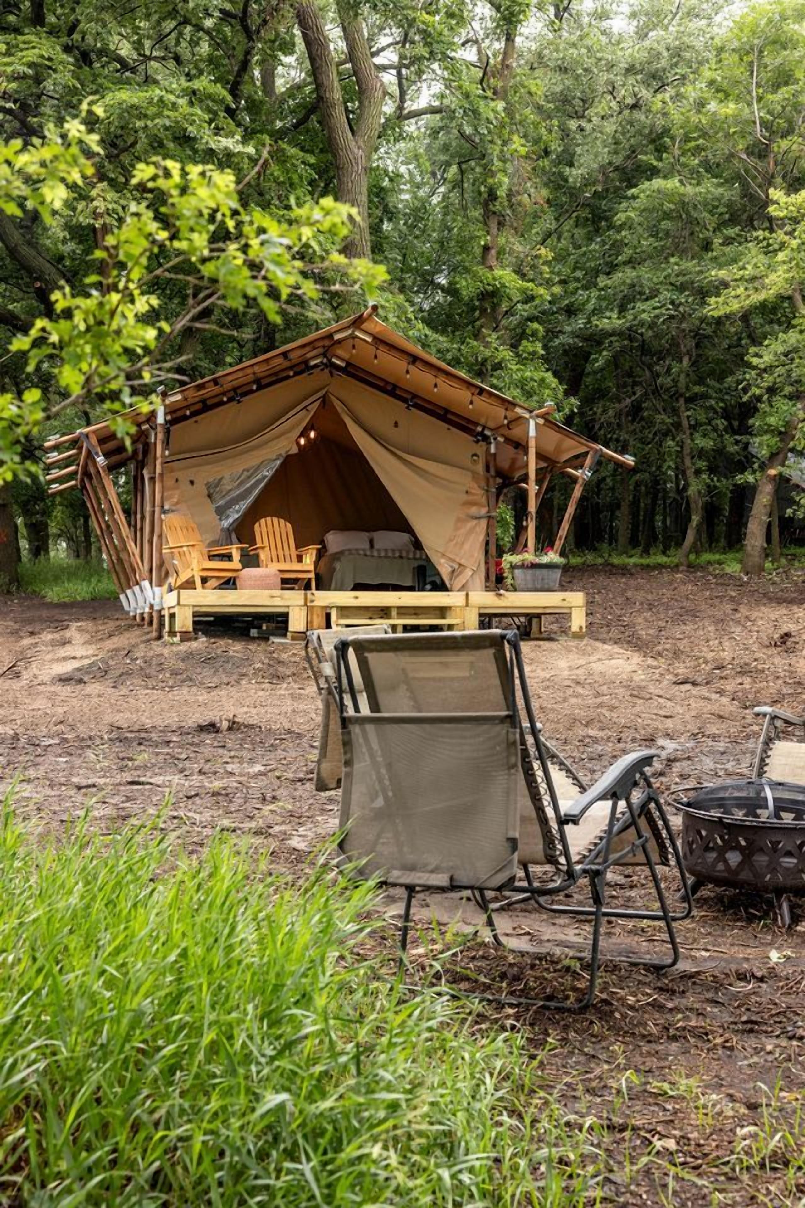 A tent with a bed, a table, and chairs set up in a forest.
