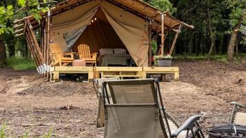 A tent with a bed, a table, and chairs set up in a forest.