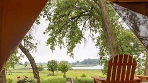 A tent with a wooden deck, a chair, and a view of a green landscape.