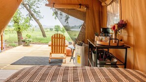 A tent with a wooden chair, a table with a coffee maker, and a view of the outdoors.