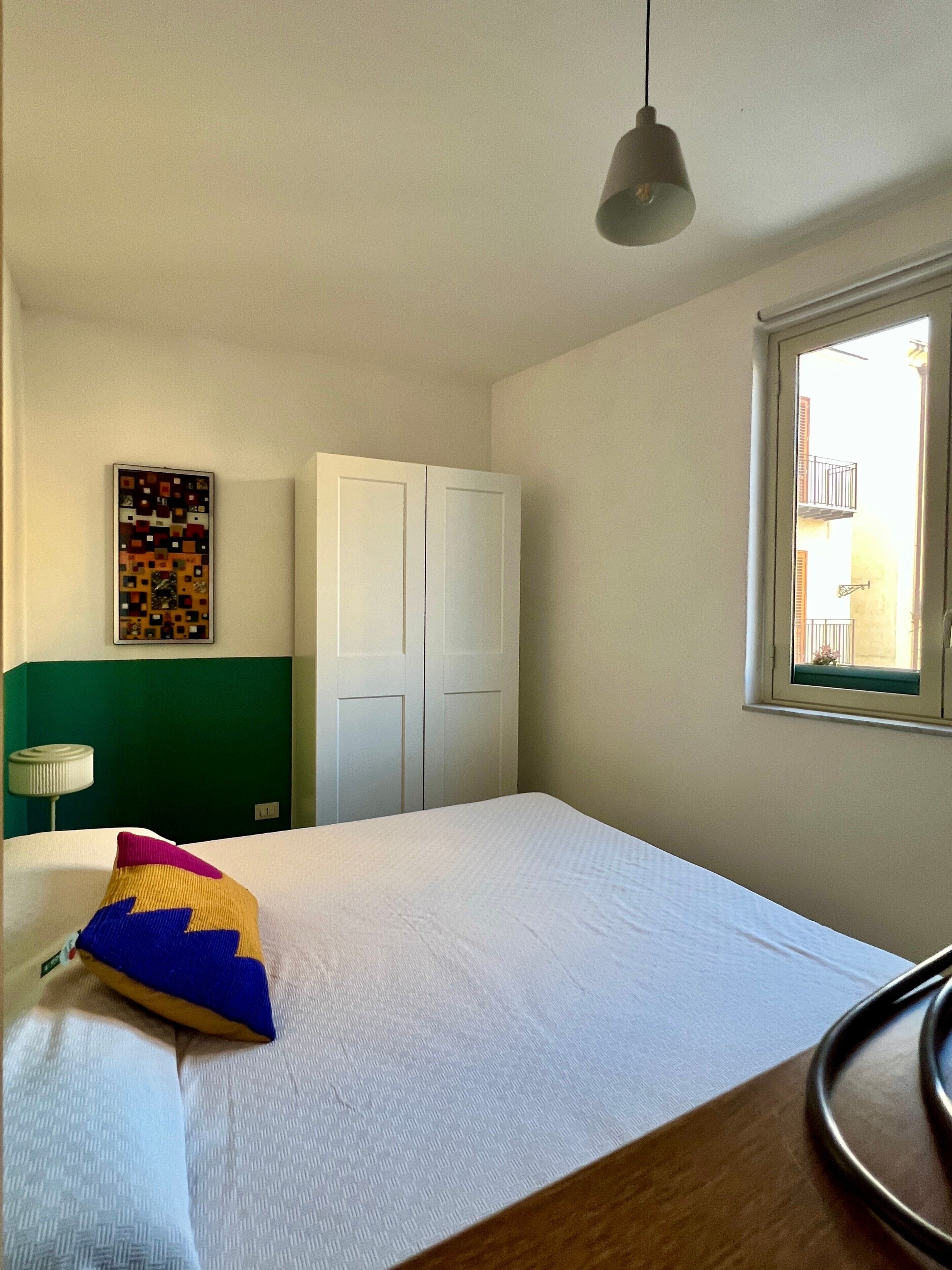 Ein Schlafzimmer mit Bett, Schrank, Fenster und einem Wandbild.