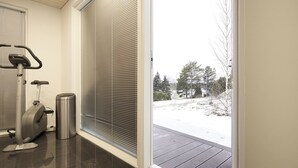 A room with a stationary bike, a trash can, and a sliding glass door leading to a snowy outdoor area. - 2BR Villa with Panorama Views - Swing A (Naantali)