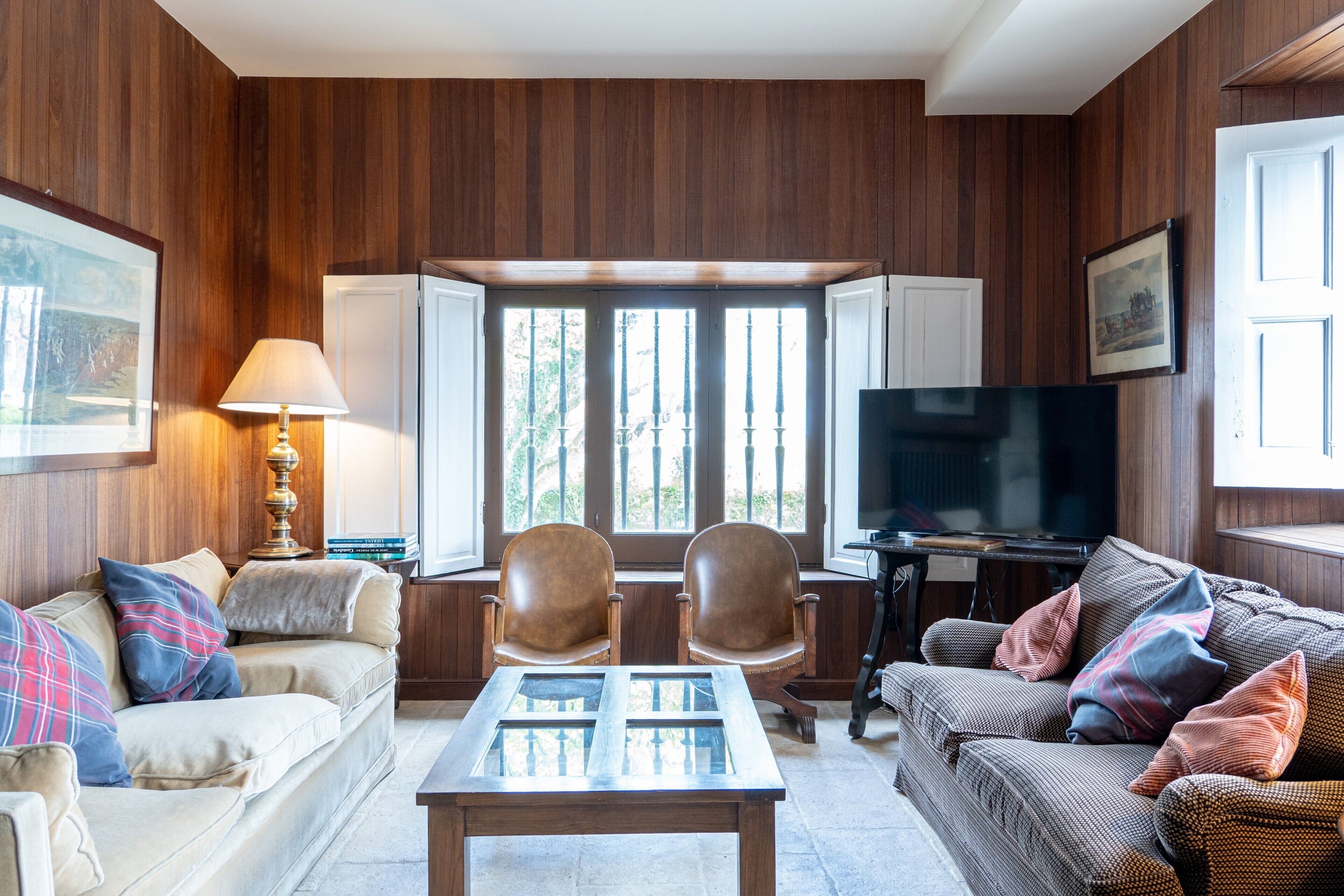Ein Wohnzimmer mit einer Couch, Sesseln, einem Couchtisch, einem Fernseher und einem Fenster mit Jalousien.
