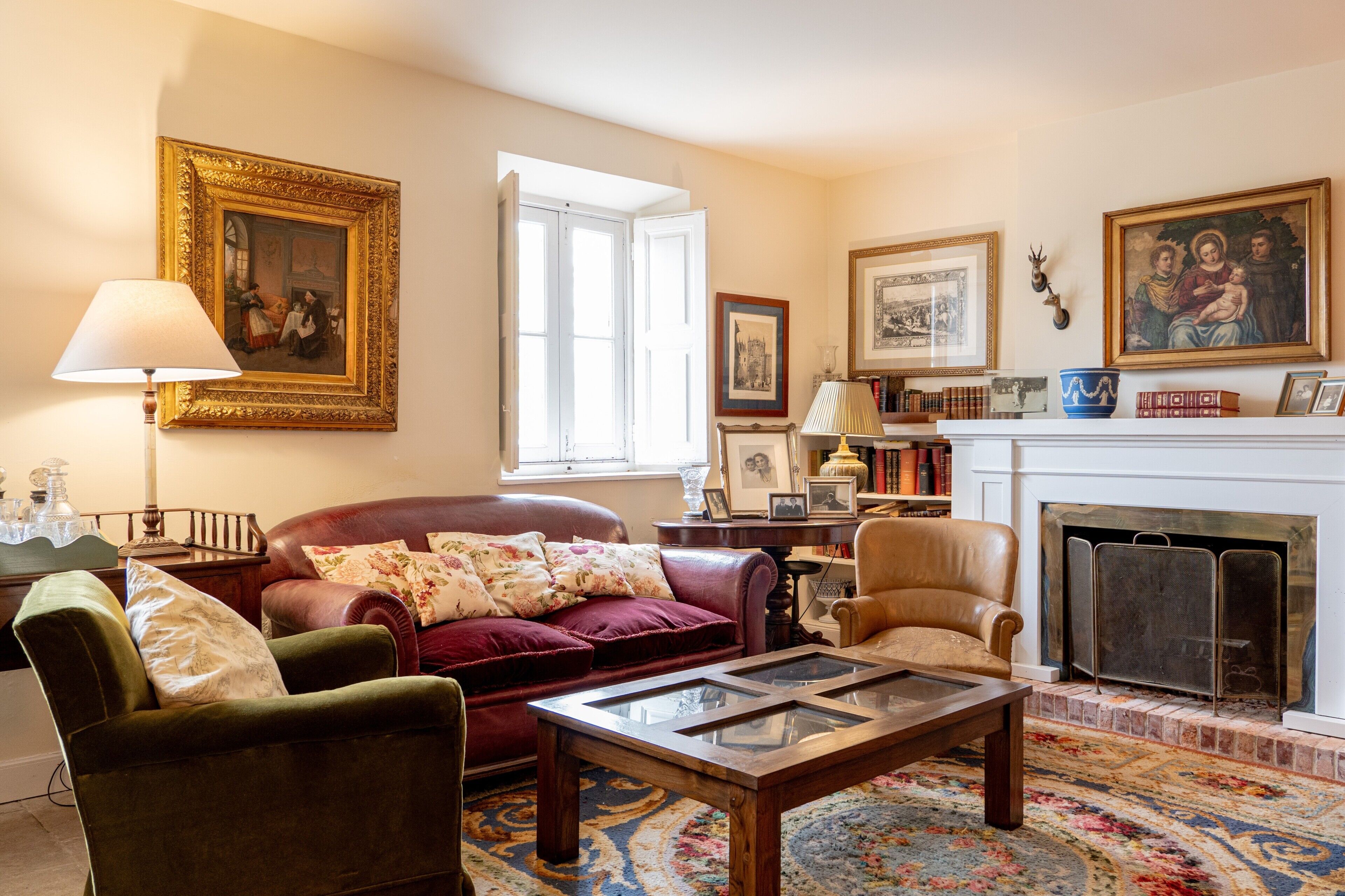 Een woonkamer met een open haard, een groene fauteuil, een rode bank en een salontafel.