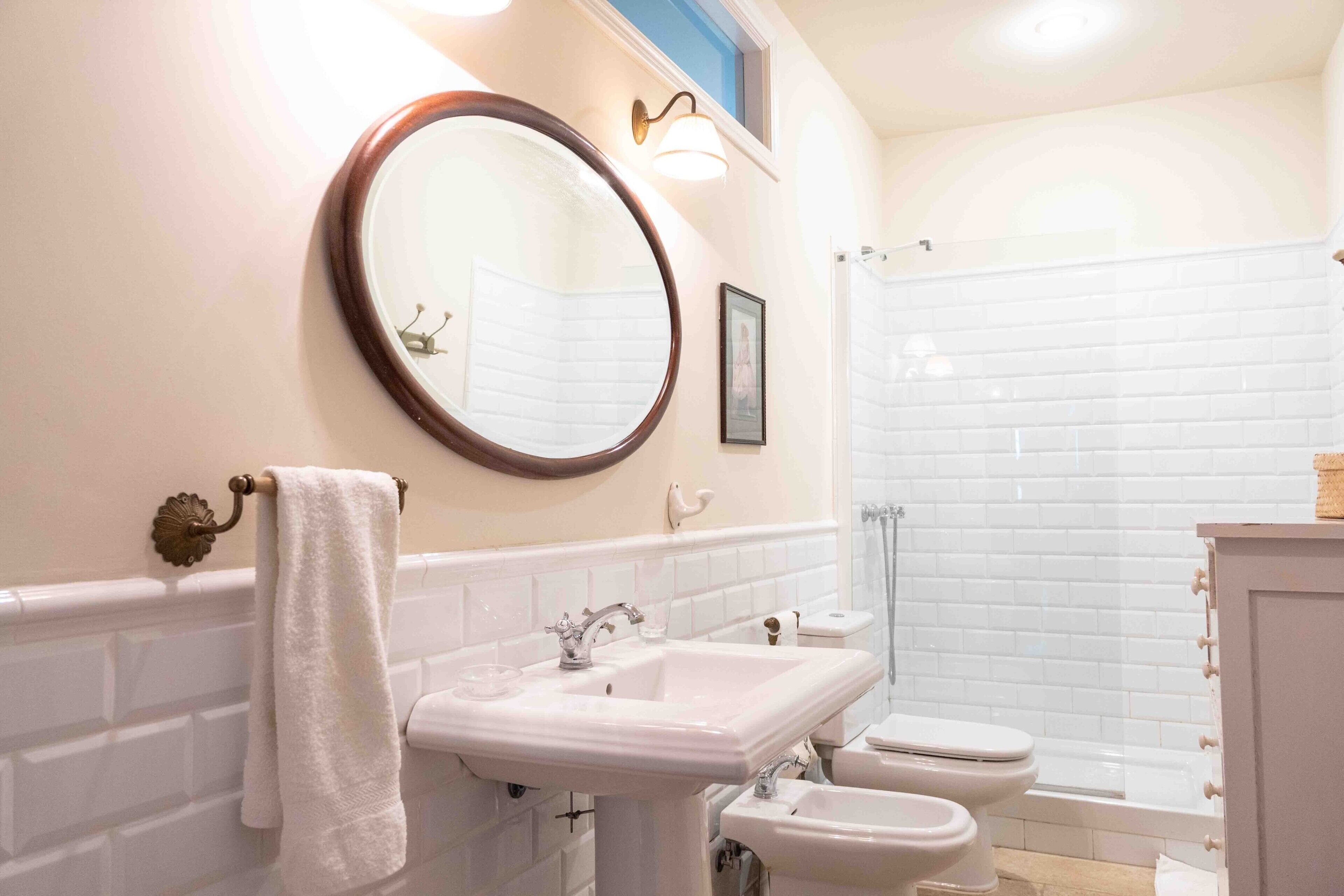 Un baño con lavamanos blanco, un espejo redondo, un inodoro y una zona de ducha.