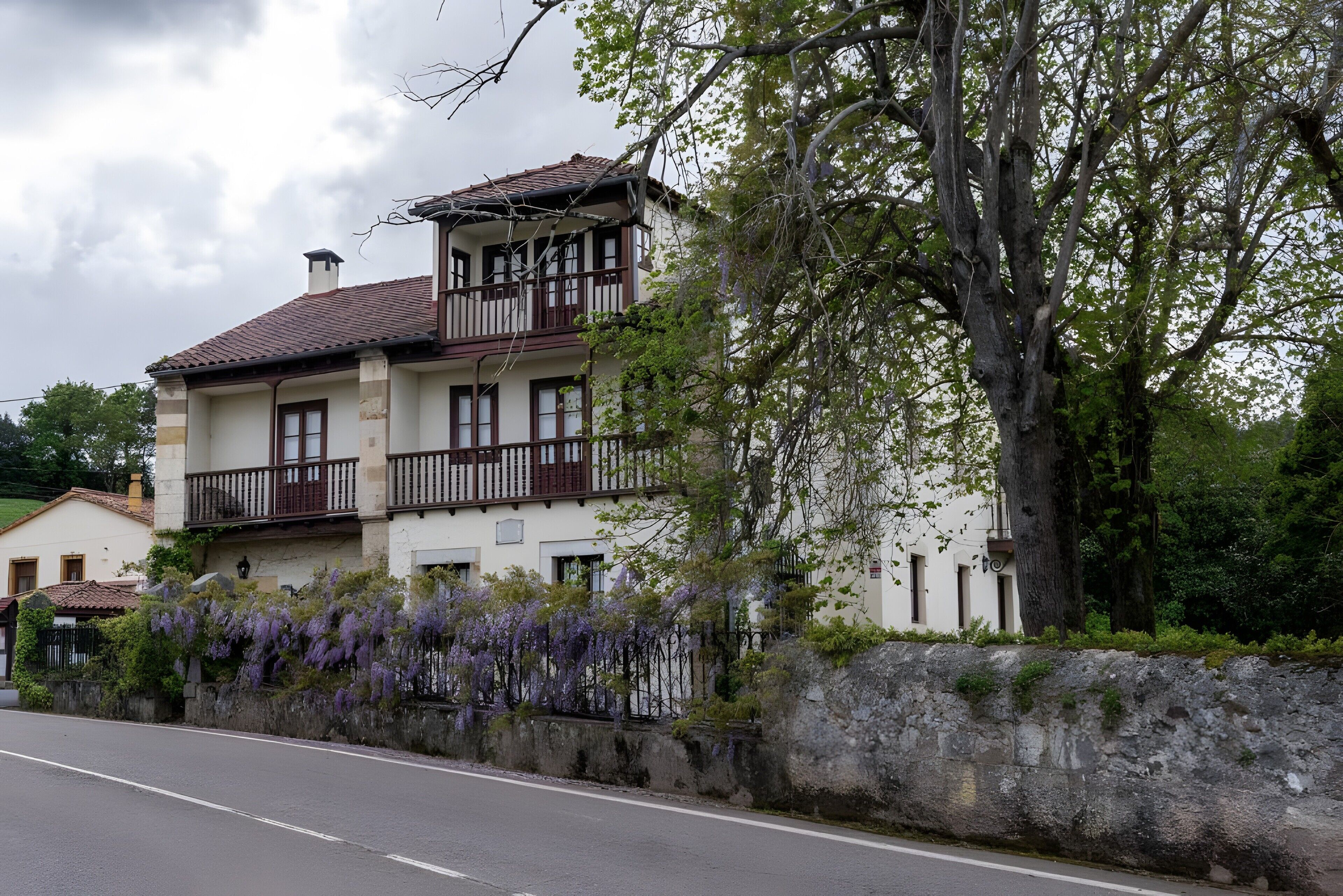 Ein zweistöckiges Gebäude mit Balkon, Steinmauer und blühenden, violetten Weinreben.