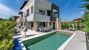 Ein modernes, zweistöckiges Haus mit Swimmingpool, Gartenmöbeln und blauem Himmel.