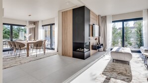 Ein modernes Wohnzimmer mit Essbereich, Kamin und großen Fenstern mit Blick auf Grünflächen.
