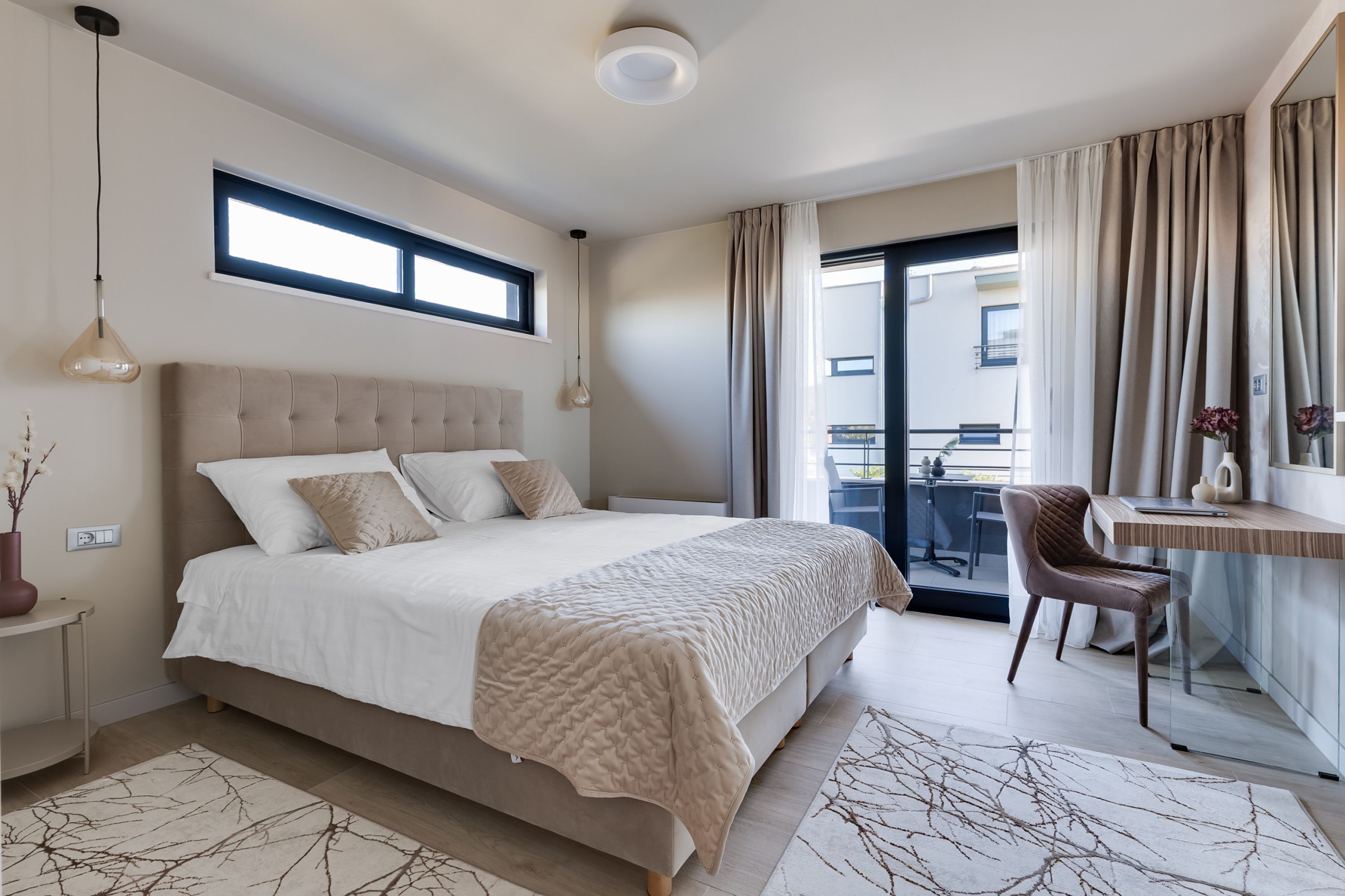 A bedroom with a large bed, a desk, a chair, a window, and a balcony.