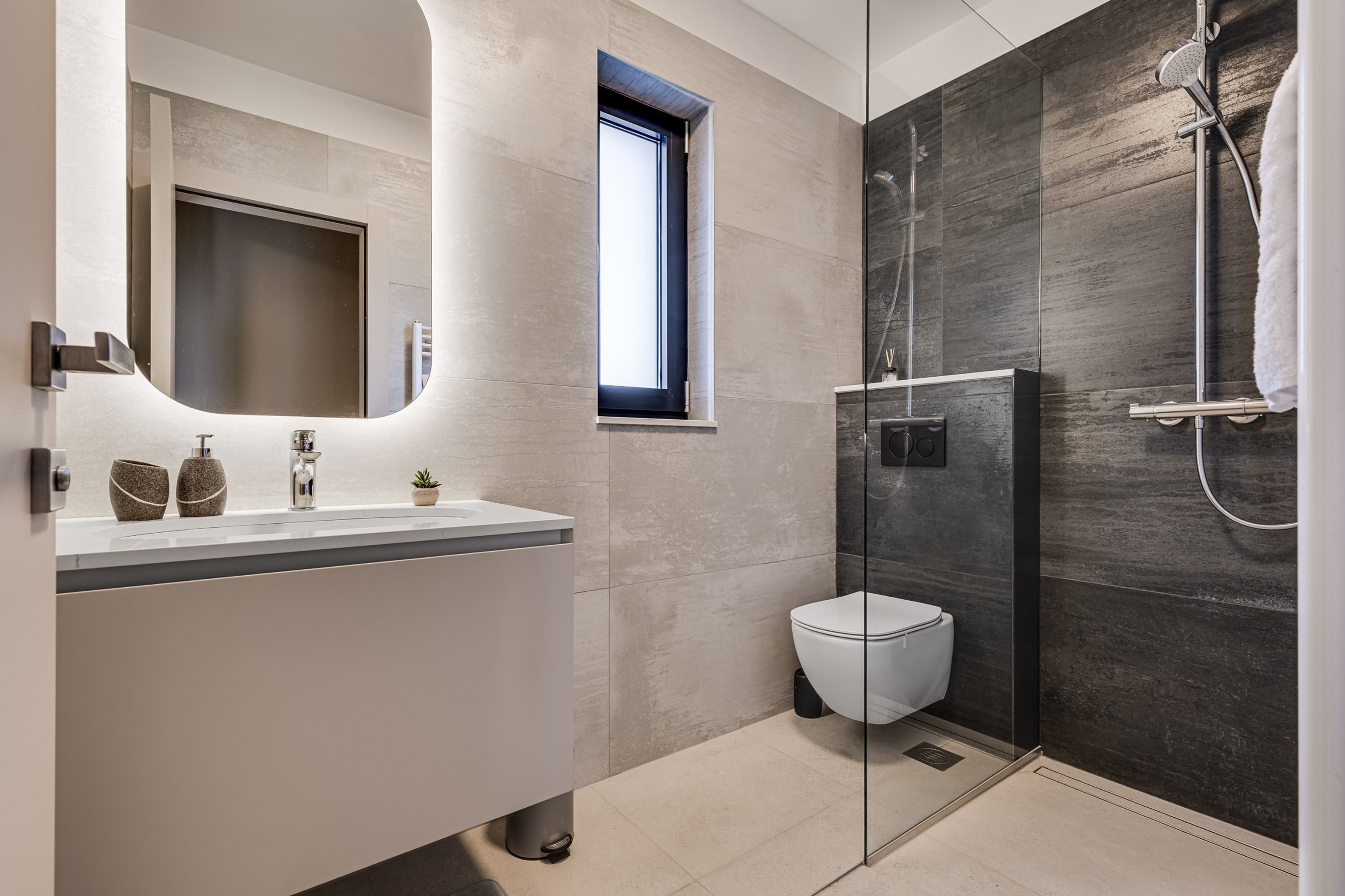 Un baño moderno con ducha envuelta en vidrio, inodoro blanco y tocador con espejo.