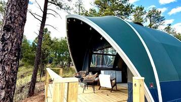 Een koepelvormige tent met een houten terras, stoelen en een tafel.