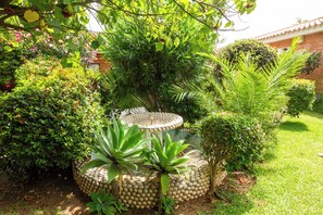 A garden with various plants, a decorative stone structure, and a brick building in the background. - 142- Oasis Villa with Private Pool & Tropical Garden close to the Beach (Benalmádena)