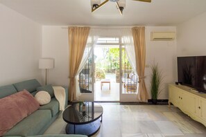 A living room with a sofa, a coffee table, a TV, and a view of an outdoor patio. - 142- Oasis Villa with Private Pool & Tropical Garden close to the Beach (Benalmádena)