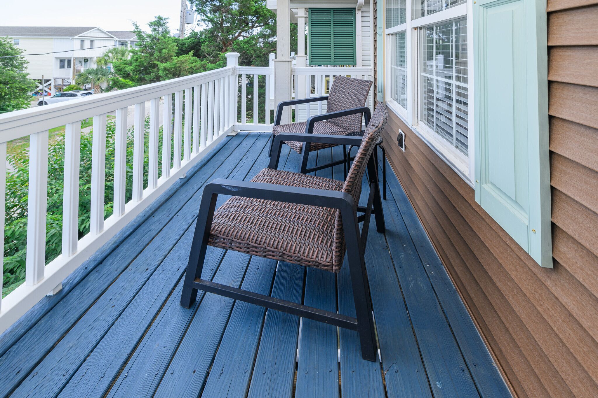 A porch with two wicker chairs, a white railing, and a view of a residential area.