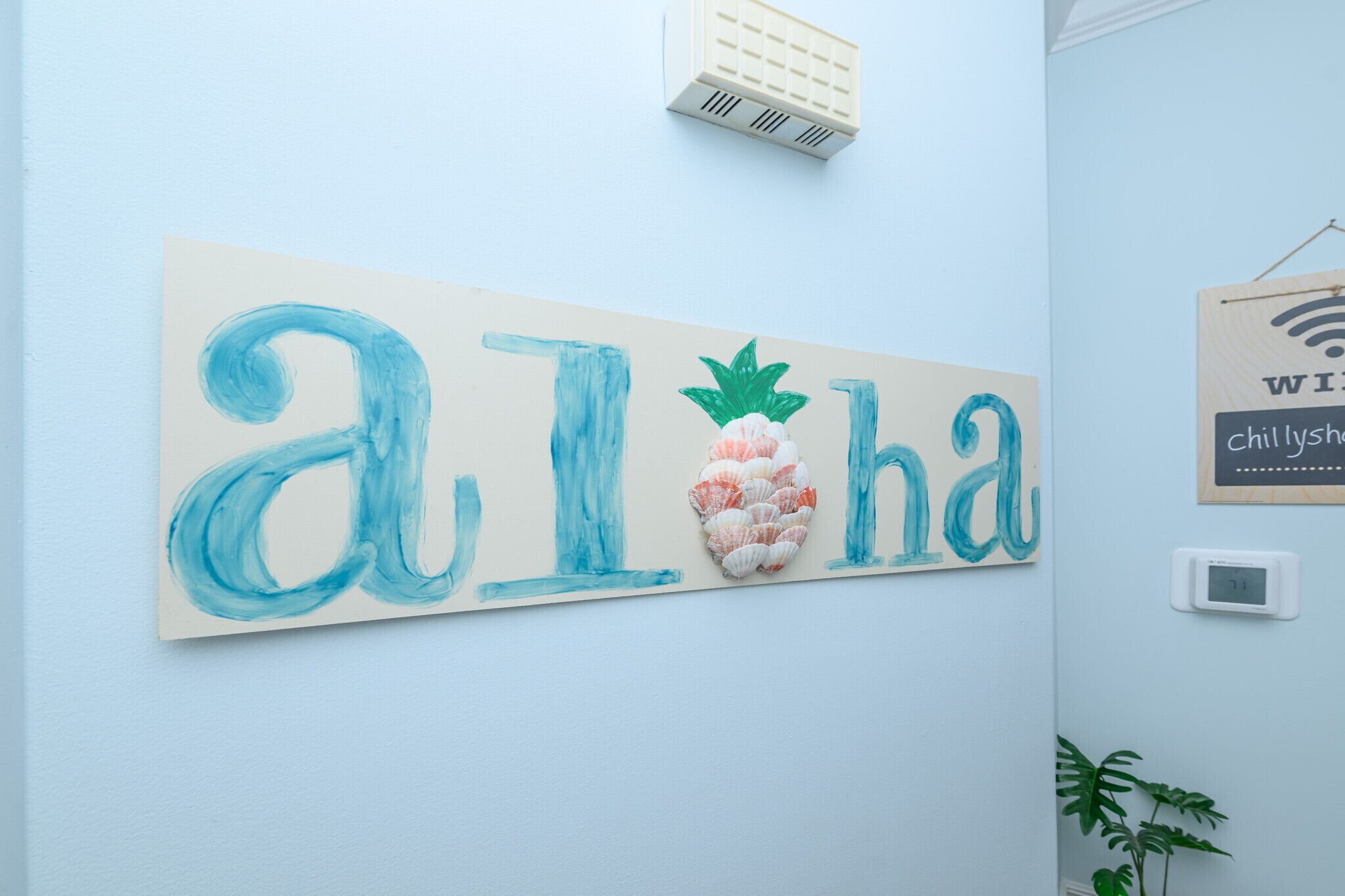 Un muro con la scritta 'Aloha' dipinta in blu, una decorazione con ananas e un simbolo Wi-Fi.