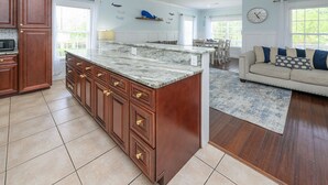Een keuken met een marmeren eiland, houten keukenkastjes en een zithoek met een bank en vloerkleed.