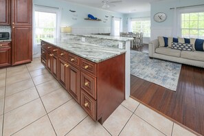 A kitchen with a marble island, wooden cabinets, and a dining area with a sofa and rug. - Walk to the Beach 4 BR with a Private Pool! Cafe Mocha (Surfside Beach)