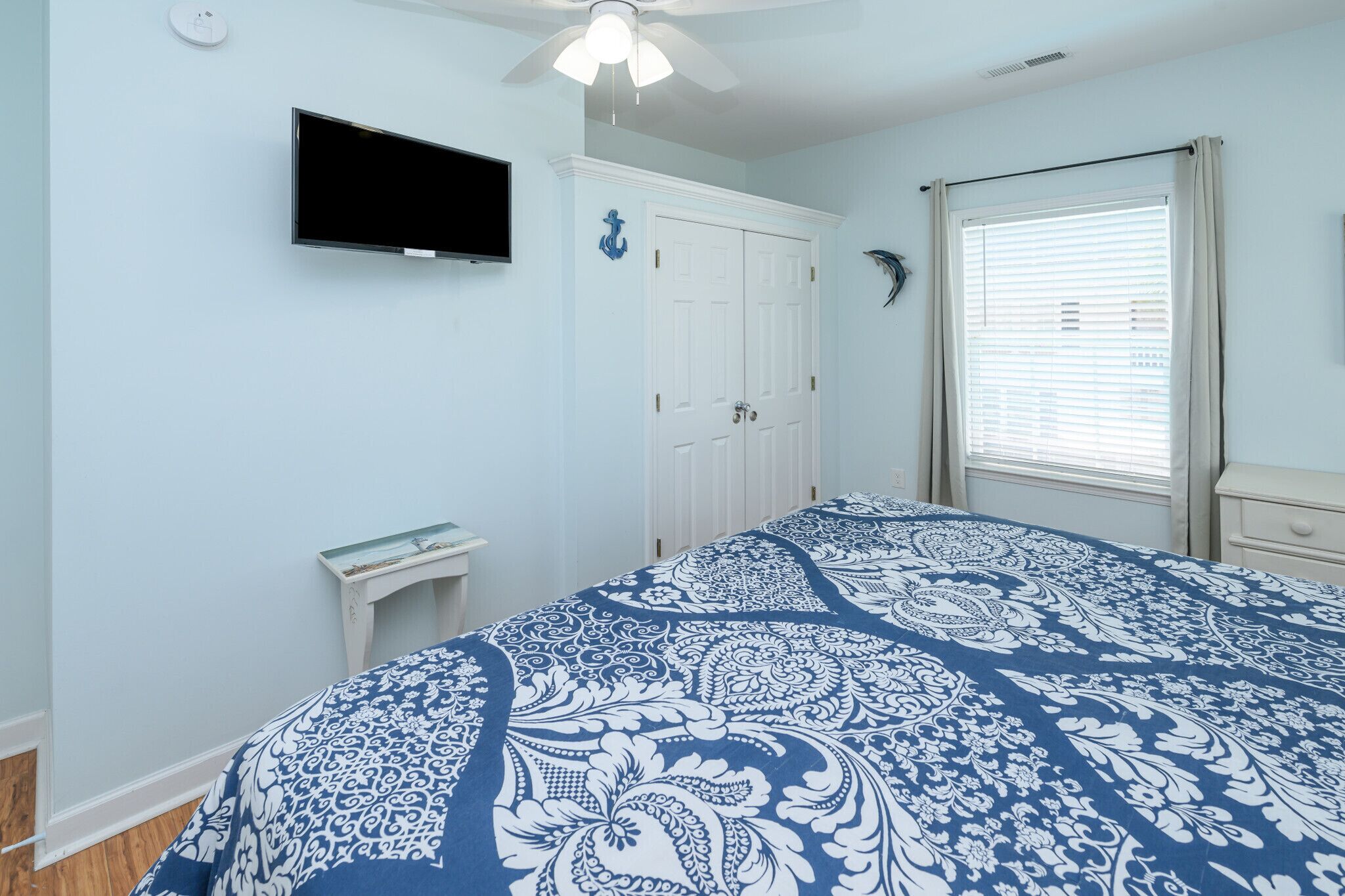 A bedroom with a bed, a TV, a door, and a window with blinds.