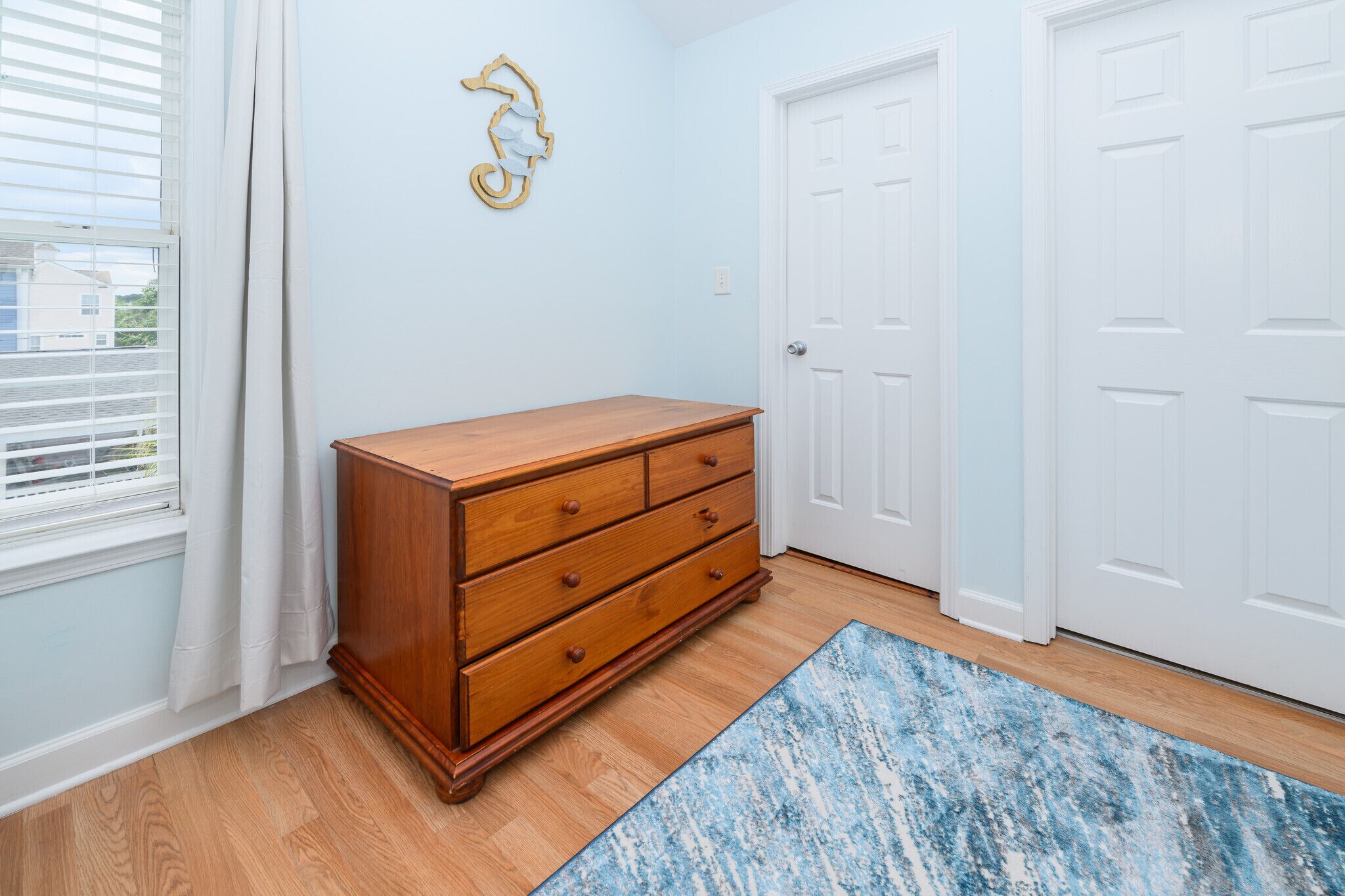 Una habitación con un aparador de madera, un tapete azul, una puerta blanca y una decoración de caballito de mar en la pared.