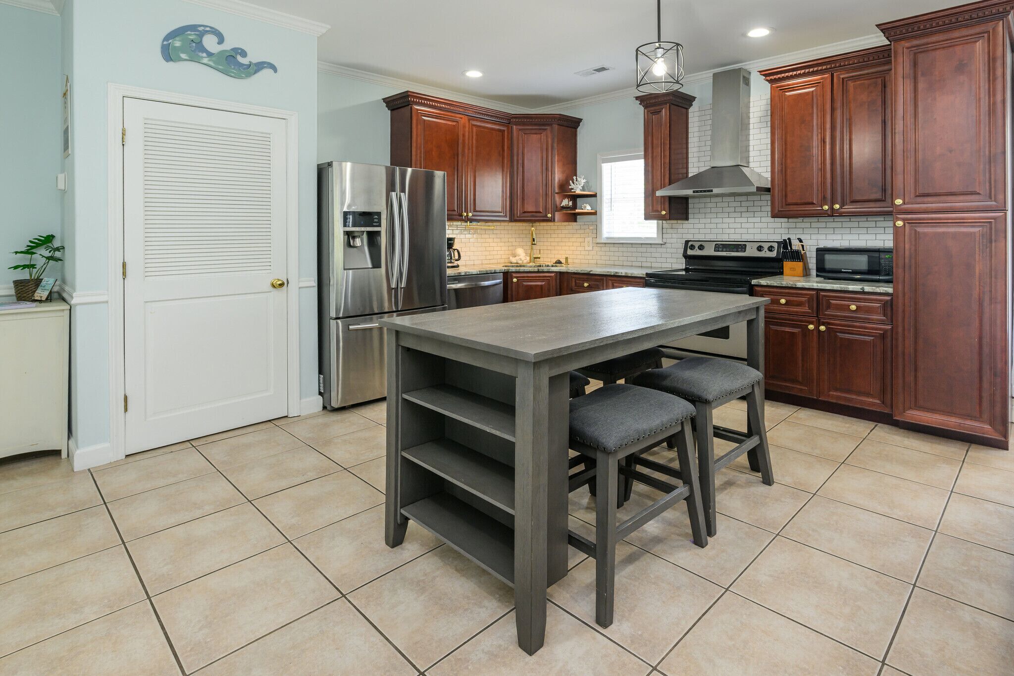 A kitchen with wooden cabinets, a stainless steel refrigerator, a built-in oven, and a grey island with bar stools.