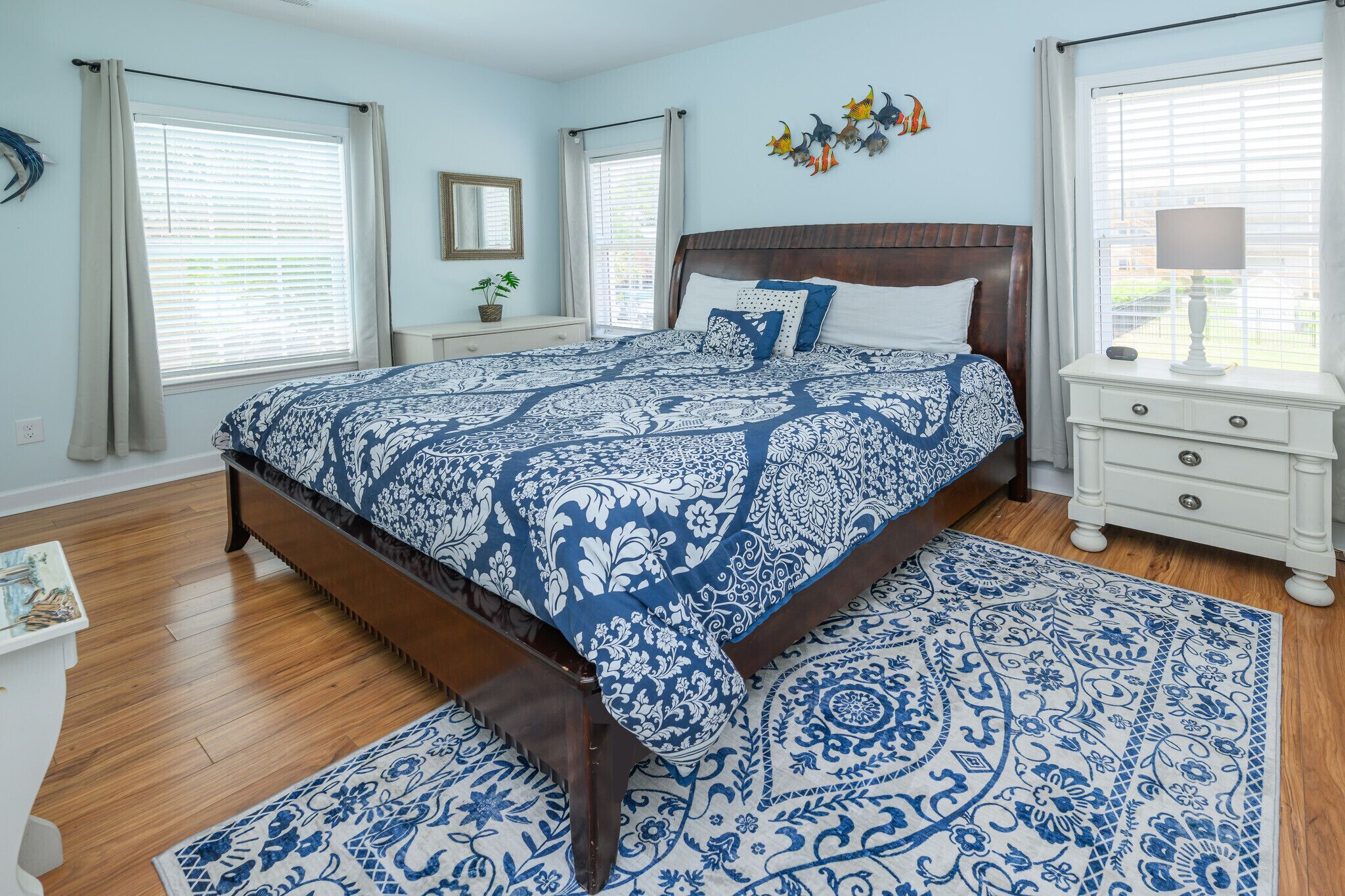A bedroom with a large bed, a nightstand, a dresser, and a window with curtains.