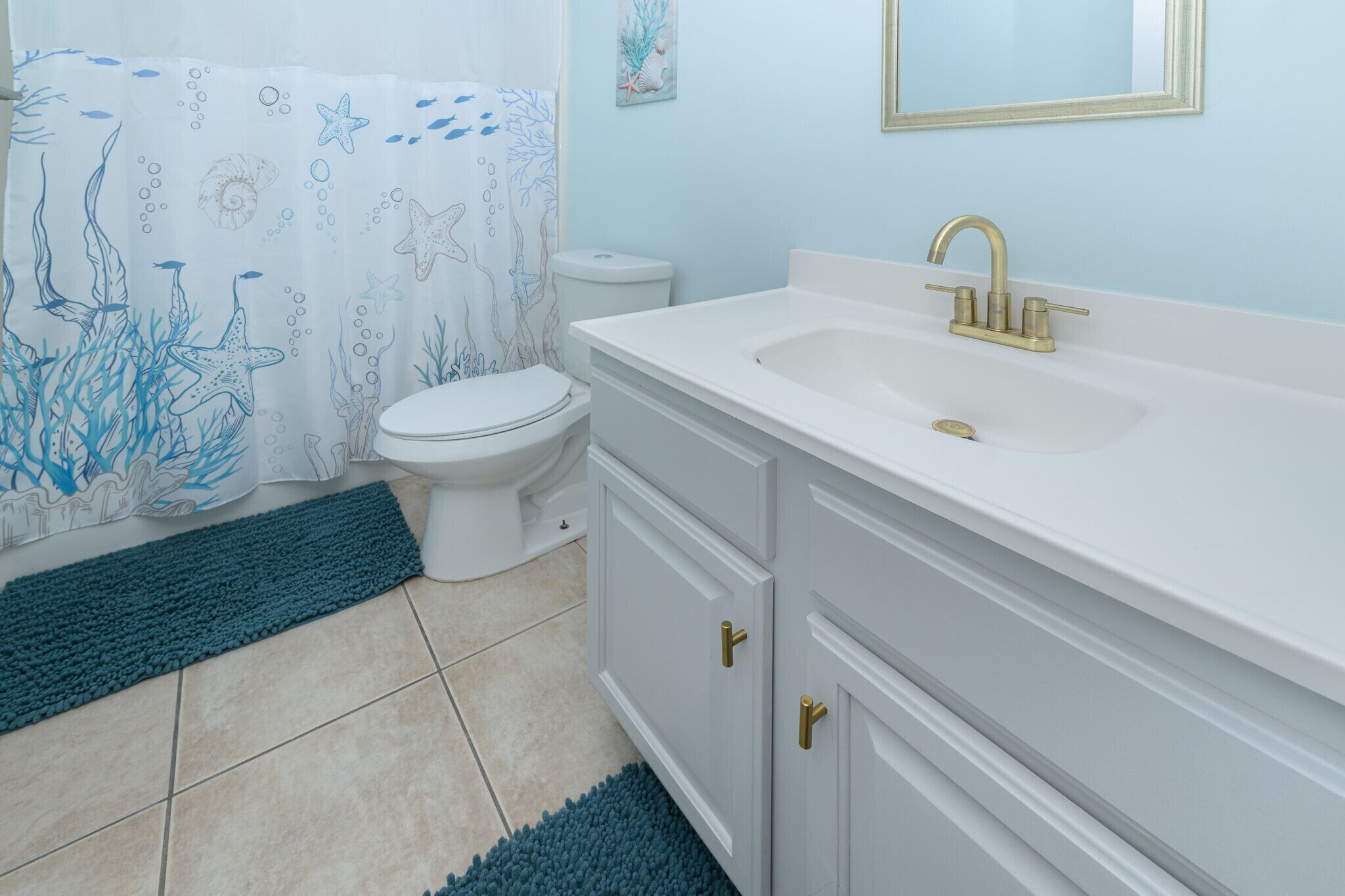 A bathroom with a white sink, gold faucet, and a toilet.