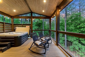 Eine Holzterrasse mit Whirlpool und Schaukelstühlen, mit Blick auf einen Wald.