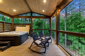 Eine Holzterrasse mit Whirlpool und Schaukelstühlen, mit Blick auf einen Wald.