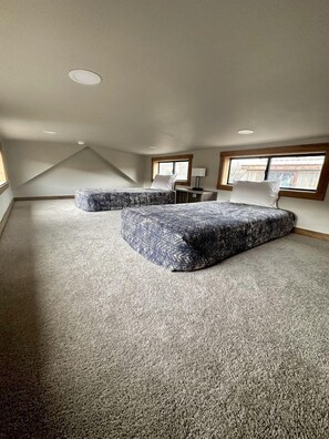 Une pièce avec un plafond en pente, deux grandes fenêtres, un lit avec une literie à motifs et un plancher recouvert de moquette.