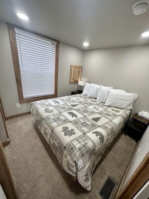 Une chambre à coucher avec un lit, une fenêtre avec des stores, une table de chevet et une lampe fixée au mur.