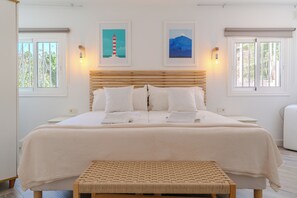 Ein Schlafzimmer mit einem großen Bett, zwei Wandleuchten, einem Kopfteil und zwei gerahmten Bildern an der Wand.