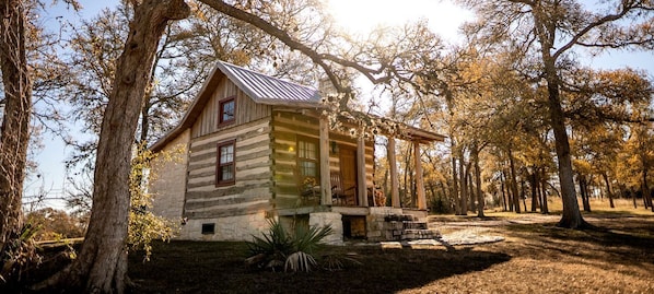 A rustic log cabin with a porch, surrounded by trees.