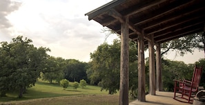 A wooden deck with a red chair, surrounded by trees and a grassy field.