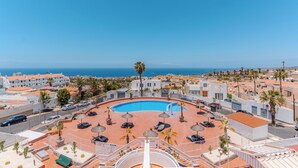 A rooftop pool with lounge chairs and umbrellas, surrounded by buildings and palm trees, overlooking a coastal area. - Charming 1-bedroom Apartment With Ocean Views in Costa Adeje (Adeje)