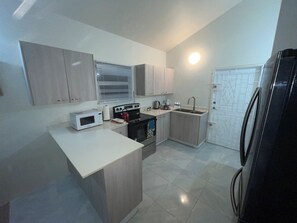 A compact kitchen with a microwave, stove, sink, and refrigerator. - Discovery Bay Villa (Discovery Bay)