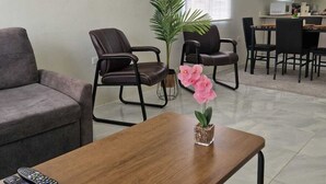 Ein Wohnzimmer mit Sofa, Sesseln, Couchtisch, Blumentopf und einem Bild an der Wand.