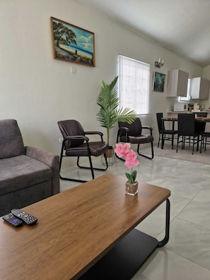 A living room with a sofa, chairs, a coffee table, a potted plant, and a painting on the wall. - Discovery Bay Villa (Discovery Bay)