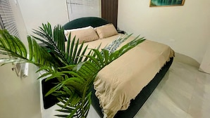Ein Schlafzimmer mit Bett, einem Topf mit Pflanze, einem Fenster mit Jalousien und einem Bild an der Wand.