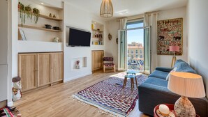 Uma sala de estar moderna com sofá, televisão, armários de madeira e uma janela ampla.