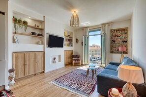 Een moderne woonkamer met een bank, televisie, houten kasten en een groot raam.