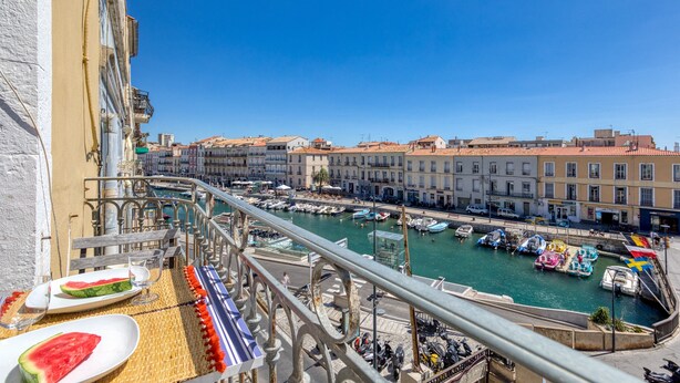 Varanda com mesa posta para refeições, com vista para uma marina com barcos e edifícios.