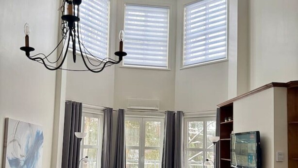 A spacious living room with a fireplace, a dining area, and a large window with blinds. - Heart of Tremblant - Johanssen, Place St. Bernard (Mont-Tremblant)