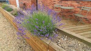 A brick house with a garden bed of lavender, a wooden deck, and outdoor furniture. - Walcott Lodges - Catley (Lincoln)