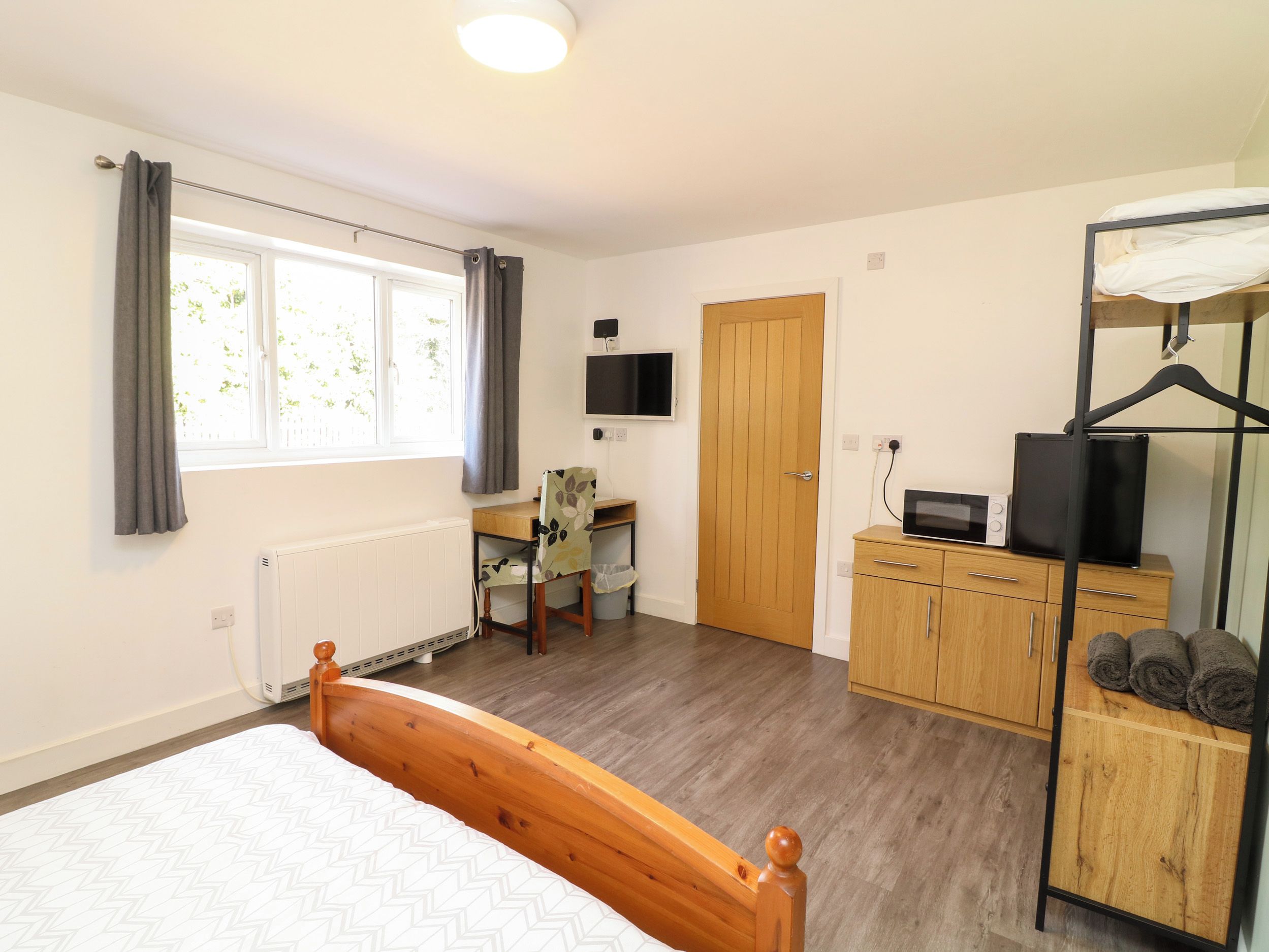 Une chambre à coucher comprenant un lit, un bureau, une chaise, une armoire, un téléviseur et un radiateur.