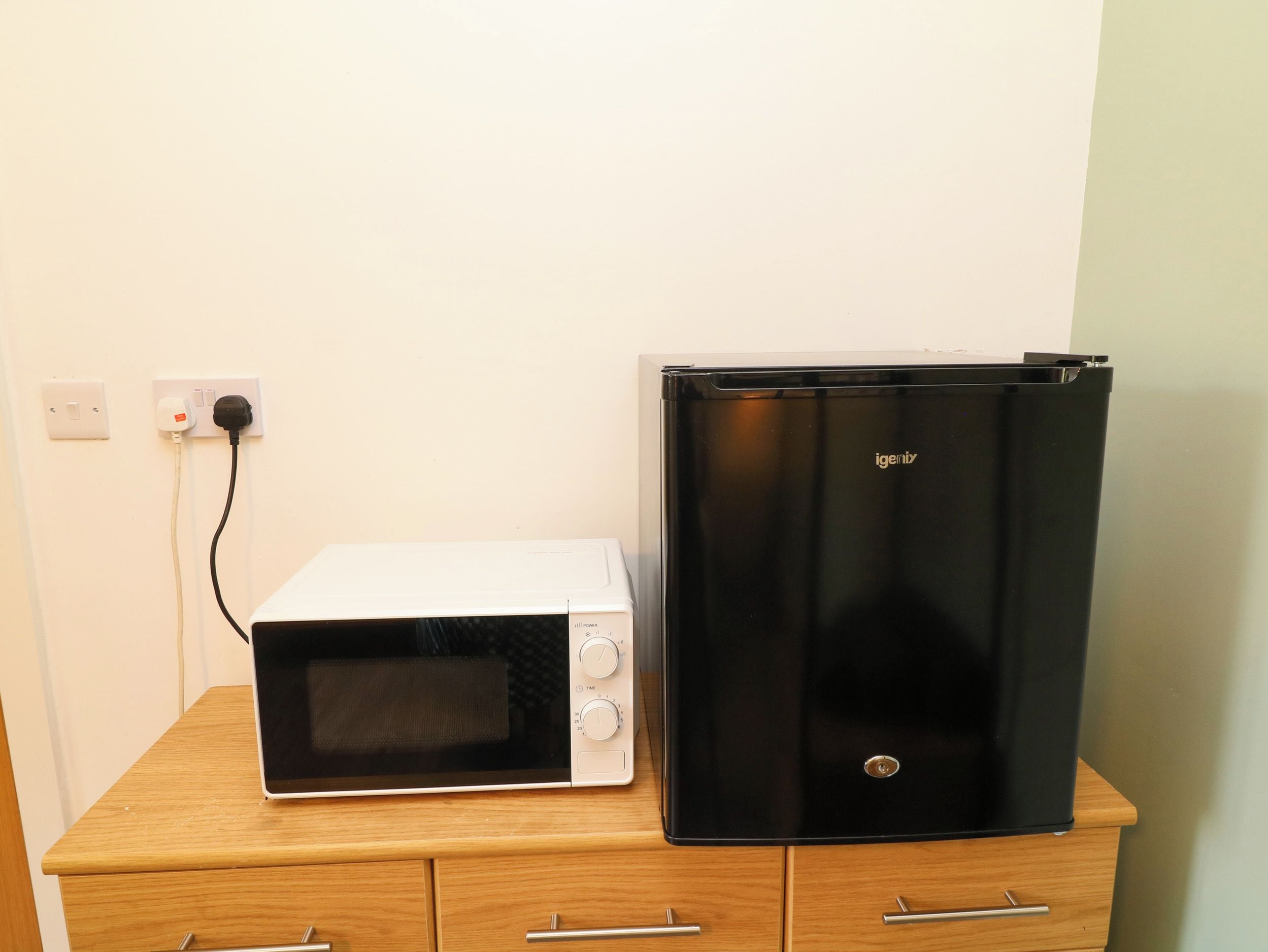 A microwave and a black refrigerator on a wooden cabinet.
